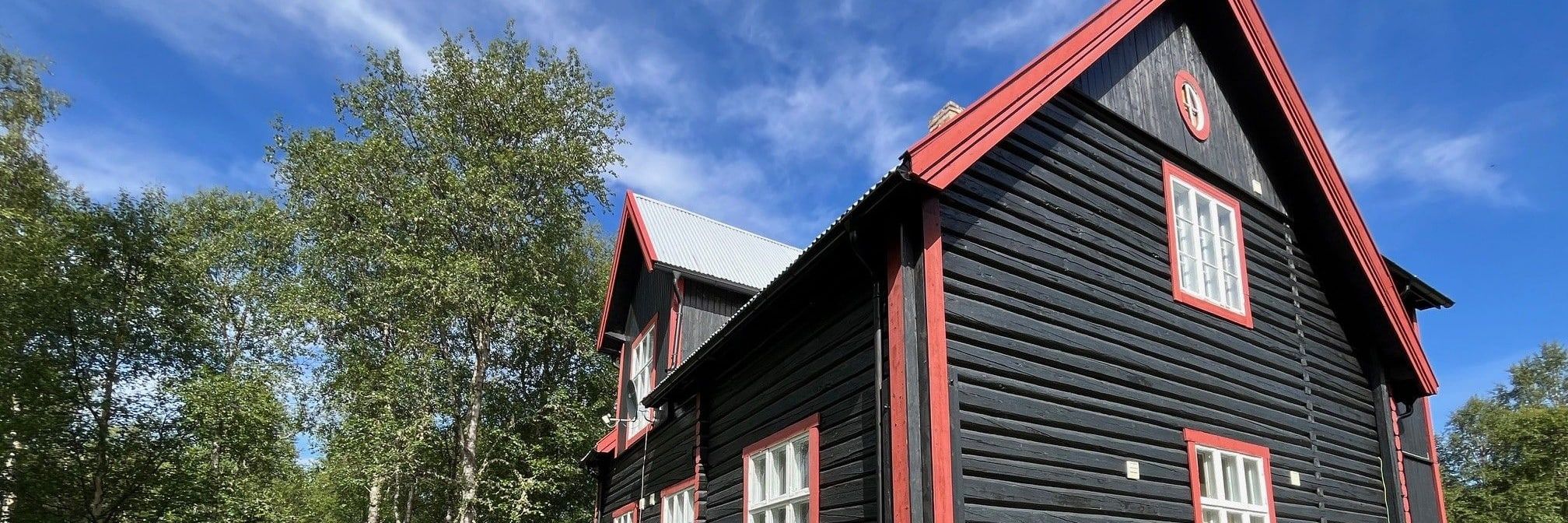 Tømmerhytta Skula fra siden en sommerdag, med bjørkeskog rundt
